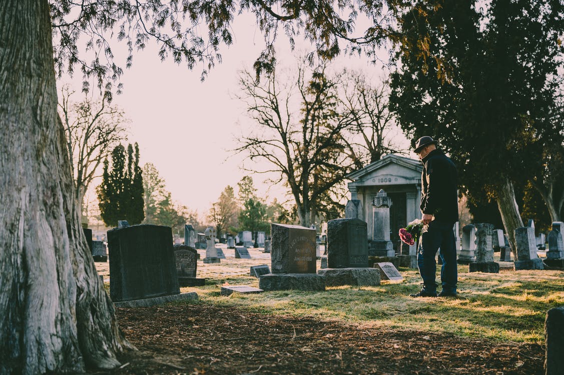 Man w/ Flowers, Looking at Tombstone in Cemetery | Make The Good Times Stop: Pop Culture’s Fixation on Eternal Oblivion | Public Square Magazine | Eternal Oblivion