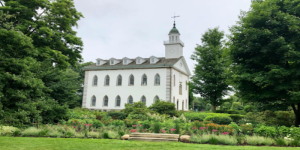 A picture of the Kirtland temple surrounded by green vegetation on a beautiful spring day.
