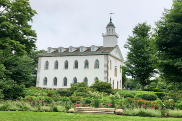 A picture of the Kirtland temple surrounded by green vegetation on a beautiful spring day.