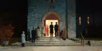 A church entryway at night with a few congregants pausing on the steps as uniformed officers stand nearby, their faces neutral, the doorway brightly lit against deep shadows. A guarded place of worship suggests canada freedom of expression and faith under legal uncertainty.