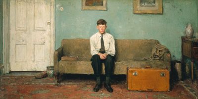 An early returned missionary sits alone in a quiet living room beside a suitcase.
