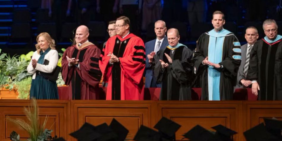 Elder Clark G. Gilbert (center), and BYU–Idaho President Alvin F. Meredith III and his wife, Jennifer (left), applaud as graduates enter the BYU–Idaho Center for commencement on Thursday, December 19, 2024. Photo by Reilly Cook, BYU–Idaho. Elder Gilbert’s call to the Quorum of the Twelve Apostles have led to questions about his commitment to BYU academic freedom.