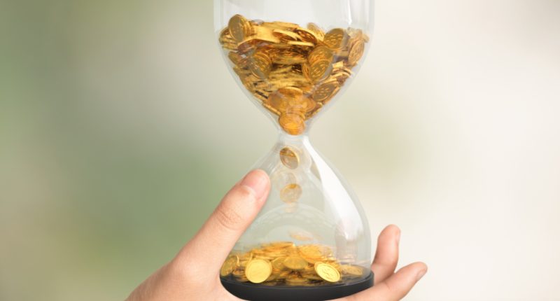 Hourglass with gold coins on hand, Time is money concept